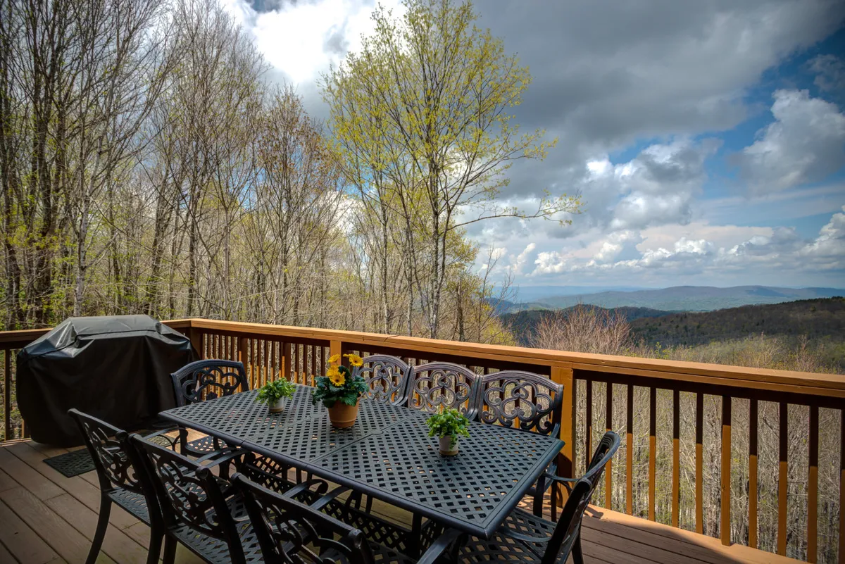 A vibrant outdoor deck scene featuring a dining table adorned with fresh flowers, a grill ready for barbecues, and sweeping mountain views beyond. The setting glows with warm, inviting light, perfect for gatherings and al fresco meals.