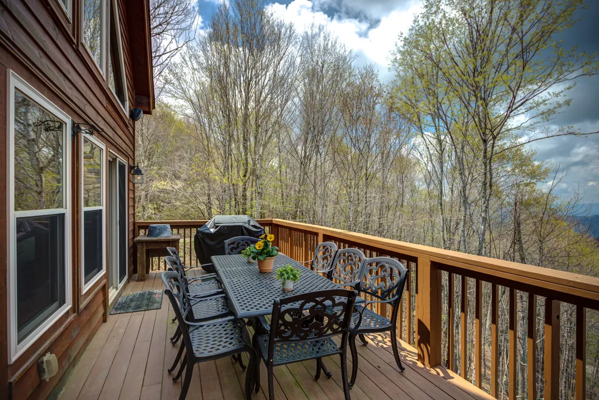 An inviting outdoor dining area with a table and chairs, a grill, and a potted flower set on a deck overlooking the trees. The setup is perfect for outdoor meals, grilling, and socializing in a serene, natural setting.