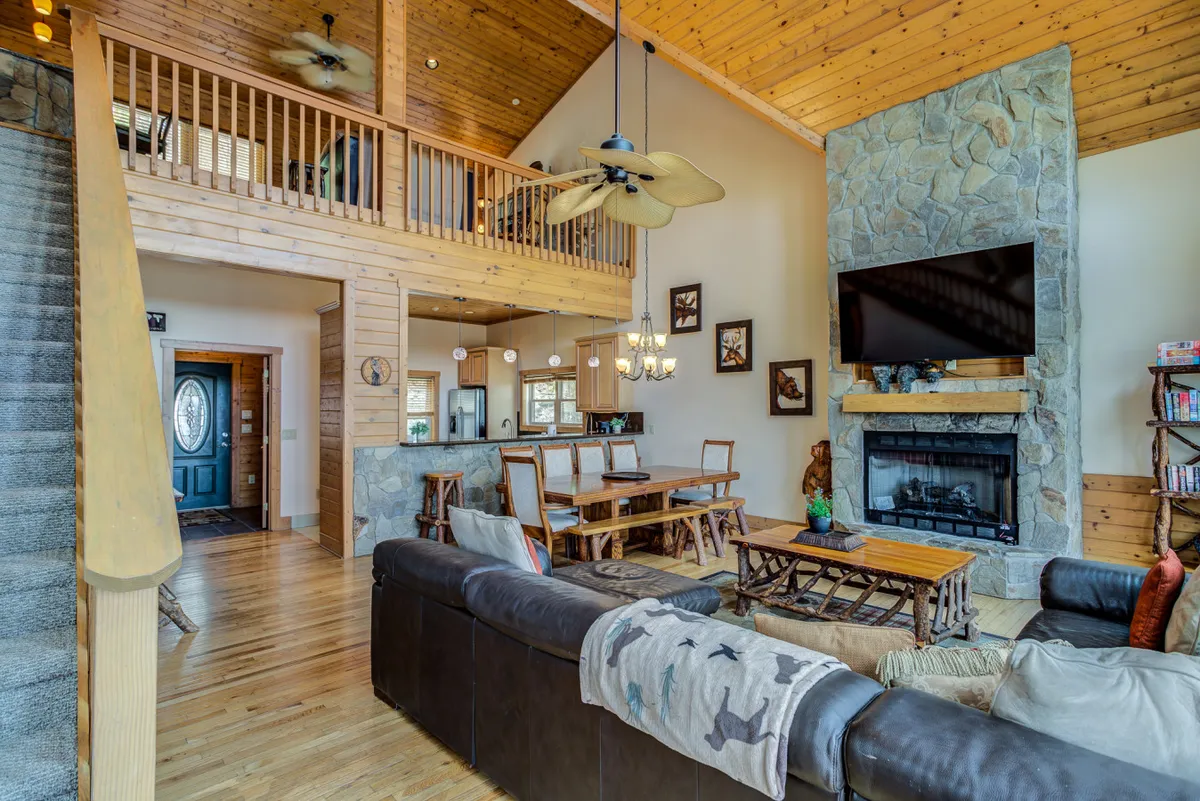 An expansive living area with a large stone fireplace, a spacious sectional sofa, a dining table, and an open staircase. The space is designed for gatherings and warmth, ideal for the entire family, including pets.