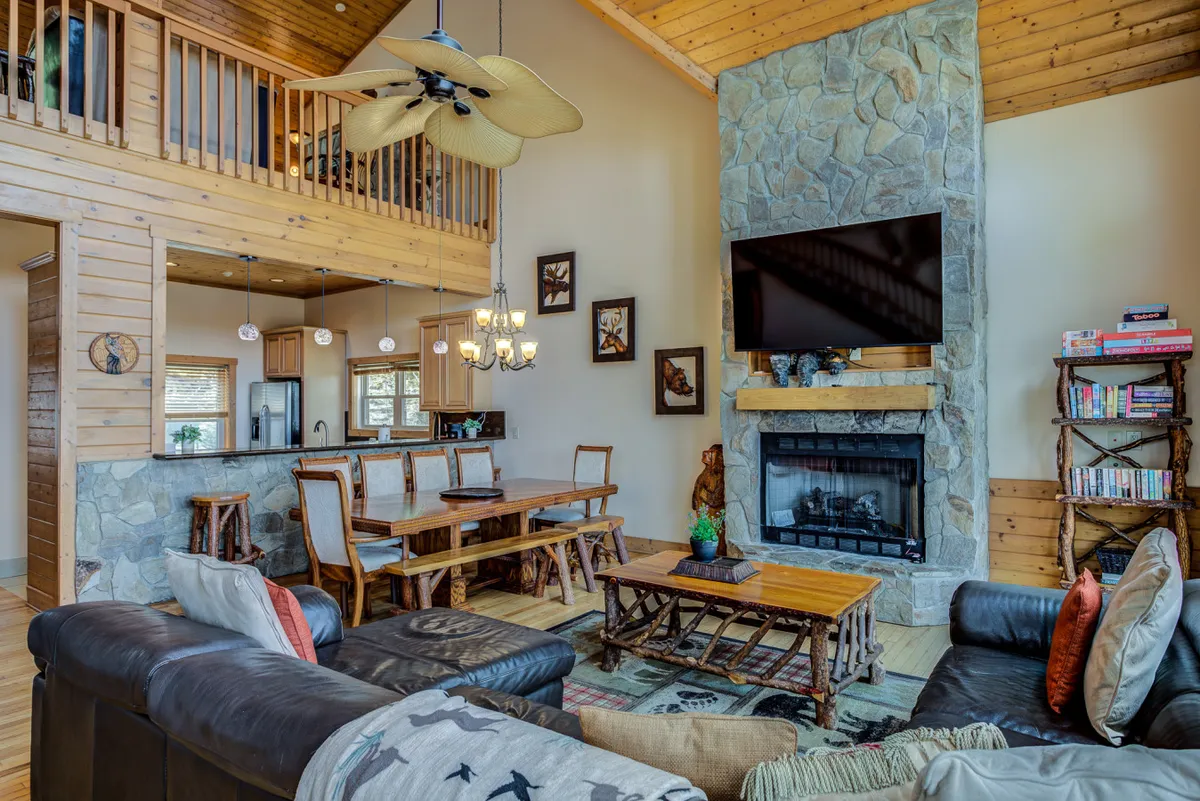 A cozy living and dining space is anchored by a prominent stone fireplace, a large leather sofa, a wooden dining table, and decorative artwork. The mood is inviting, suggesting opportunities for family gatherings, relaxation, and shared meals in a welcoming setting.