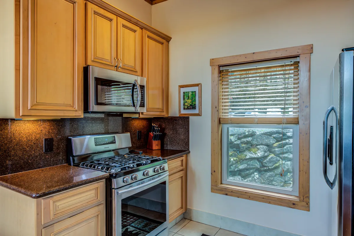 A bright, fully stocked kitchen is the focal point here, featuring stainless steel appliances, granite countertops, wooden cabinetry, and a window with a view. The setup radiates warmth and functionality, ideal for group meal prep and socializing.