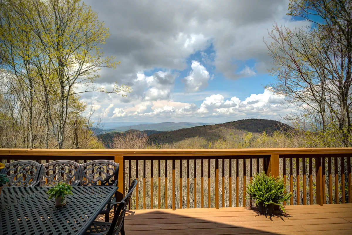 This exterior image features a spacious dining table set on a deck with a stunning mountain view, decorative plants, and a sturdy railing. The scene is inviting for group gatherings, morning coffee, or sunset dinners, encapsulating the experience of enjoying food and company amid nature.