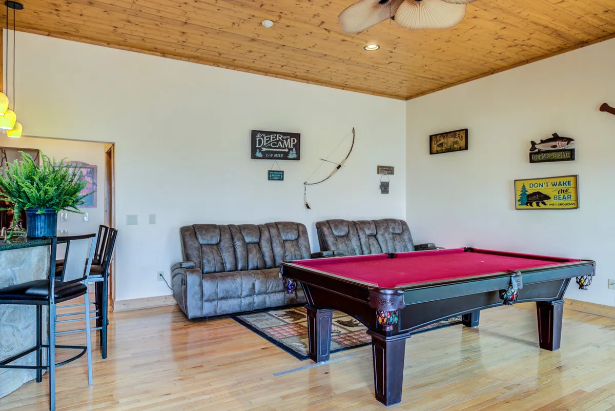 A cozy game room featuring a classic pool table surrounded by comfortable seating, warm wooden accents, and decorative signage. The relaxed lighting and friendly ambiance make it ideal for lively gatherings or unwinding after outdoor adventures.
