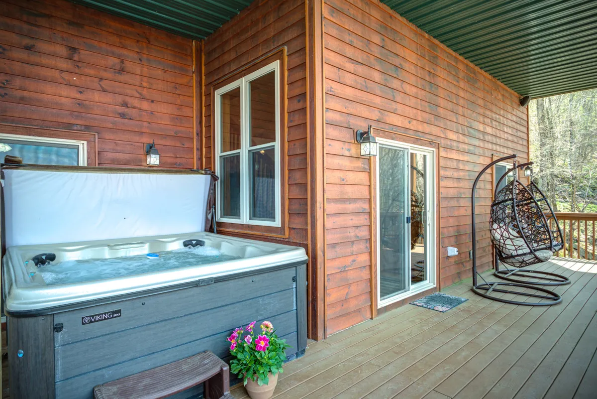 A wooden deck featuring a hot tub, hanging chair, and flower pot, framed by surrounding trees. The setup is inviting for both relaxation and social gatherings, with enough open space for pets to roam safely while their owners soak or enjoy the deck.