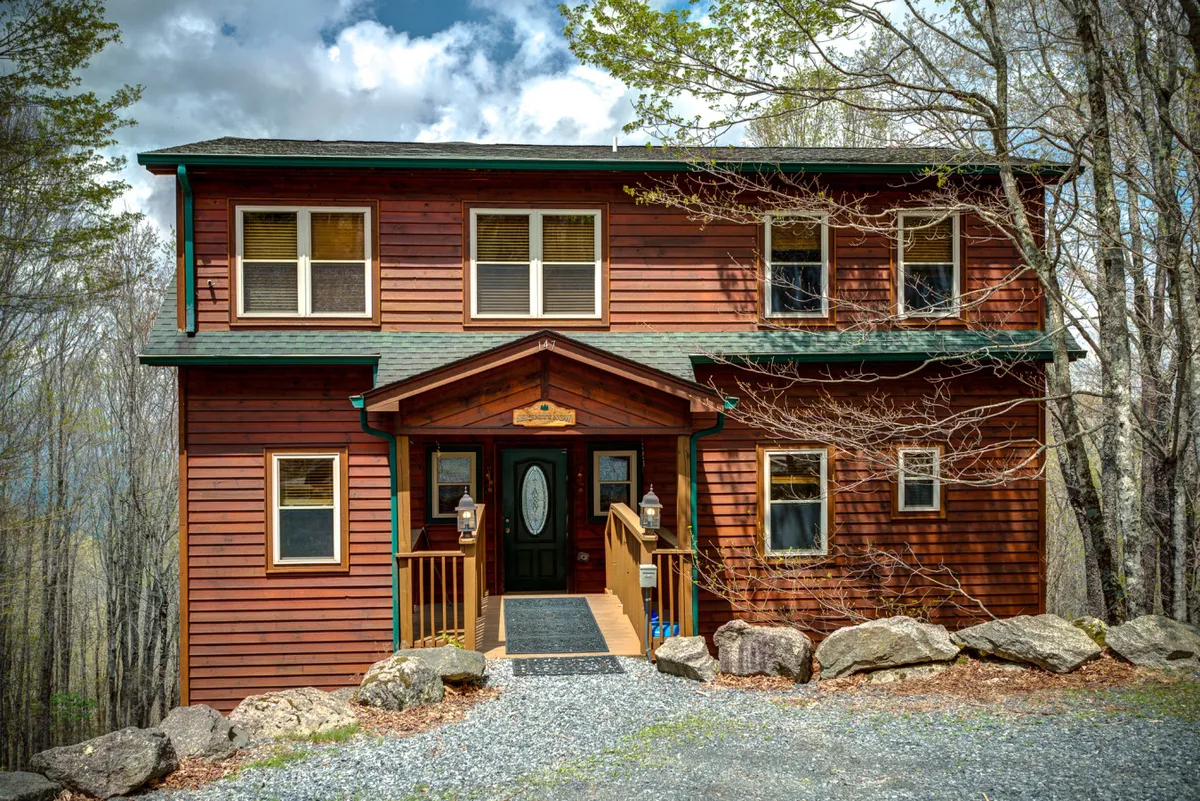 The welcoming front porch of Serenity Lodge, featuring a sturdy wooden door and stone pathway nestled among mature trees. The scene hints at immediate access to nature and trails, with an inviting transition from the lodge to the outdoors.