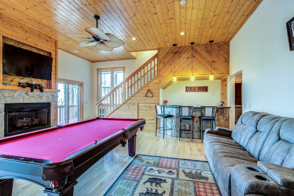 A cozy, inviting game room interior with a pool table, fireplace, bar area, and comfortable seating. The atmosphere is casual and perfect for group gatherings or friendly competition after outdoor adventures.