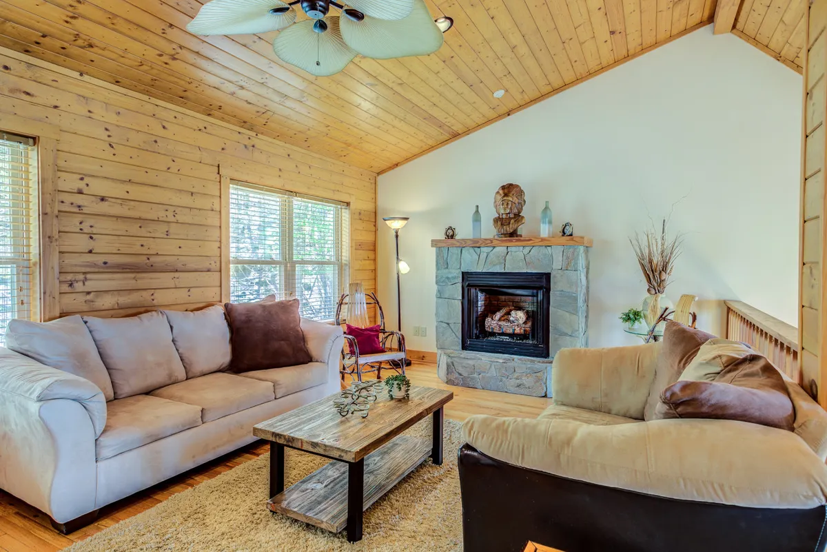 A cozy living room featuring a plush sofa, a warm fireplace as the focal point, a coffee table, and a window allowing natural light to filter in. Decorative items create a welcoming, homey atmosphere, perfect for family relaxation.