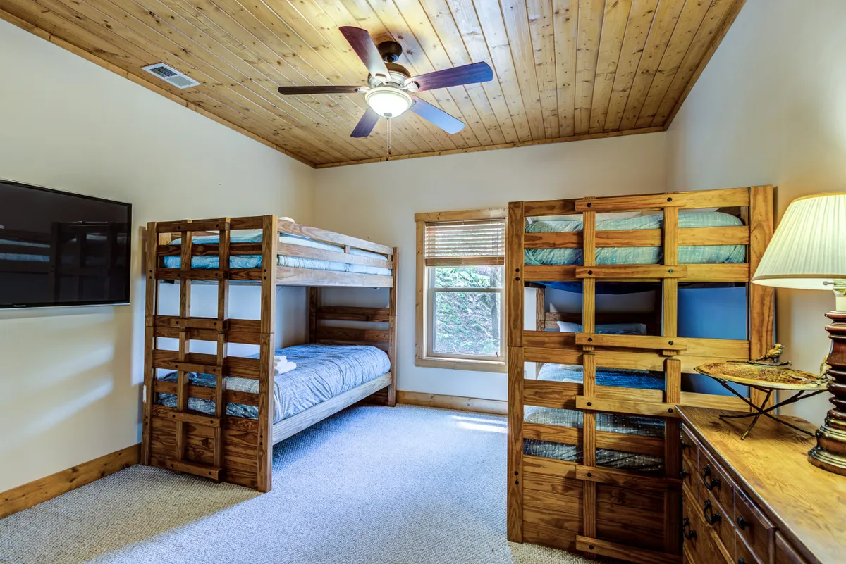 A playful bedroom space with bunk beds, a ceiling fan, window for natural light, a TV, and a dresser. The room feels bright and functional, suited for children or multi-generational guests.