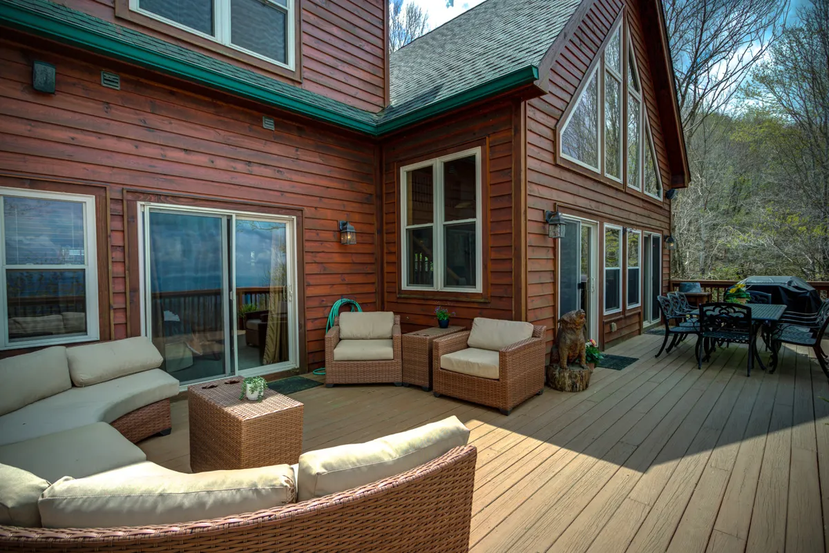 An inviting outdoor deck with comfortable seating and a dining table, set against large windows and surrounded by trees. The space is perfect for relaxing or dining al fresco while enjoying nature.